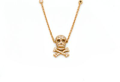 un collier représentant un crâne et des os croisés dorés sur fond blanc