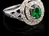 un gros plan d'une bague en diamant verte et blanche posée sur une surface noire