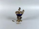 une coupe ancienne en argent et verre bleu, accompagnée d'une cuillère, posée sur une surface blanche