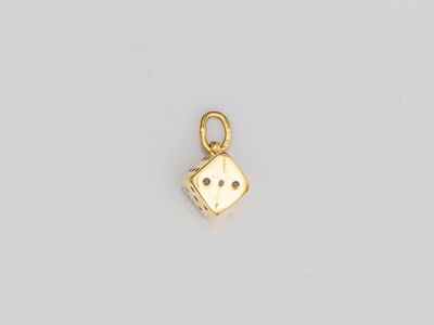un petit pendentif en forme de dé doré sur fond blanc