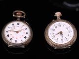 two silver pocket watches sitting next to each other on a black surface