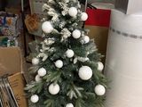 un petit sapin de Noël décoré de boules blanches et recouvert de neige