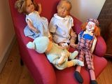 three dolls sitting on a red chair in a living room