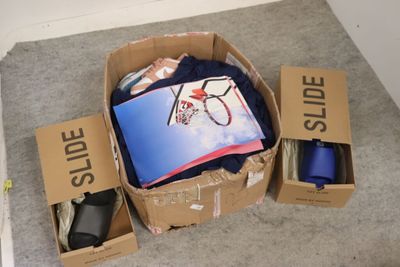 une boîte en carton remplie de vêtements et d'autres objets, posée par terre