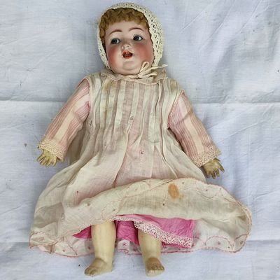 une vieille poupée avec un bonnet et une robe posée sur un drap blanc