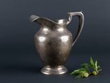an antique silver pitcher with a sprig of mint on a black background