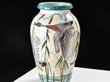 a vase that has a bird on it sitting on a table