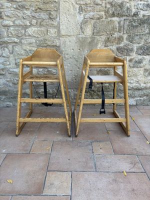 two wooden high chairs sitting next to a stone wall