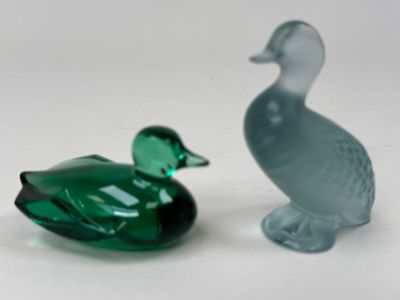 two glass ducks sitting next to each other on a white surface