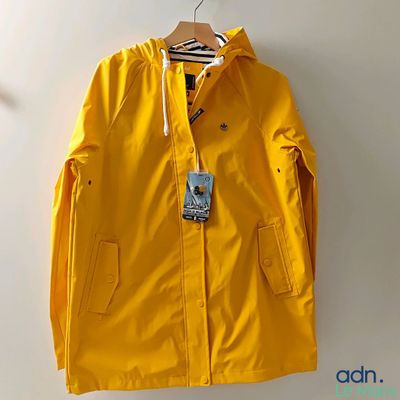 une veste de pluie jaune suspendue à un cintre sur un mur blanc