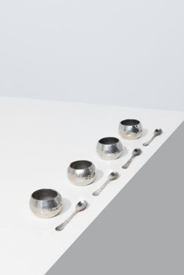 four silver bowls and spoons sitting on a white surface