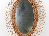 an oval mirror with a wicker frame hanging on a wall