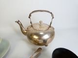 a silver teapot sitting on top of a table next to a plate