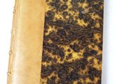 an old book with a brown and black cover sitting on top of a white table