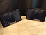 two tablet computers sitting on a table with a person taking a picture of them