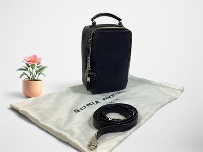 Le petit sac noir se trouve à côté d'une petite fleur rose et d'un sac blanc.