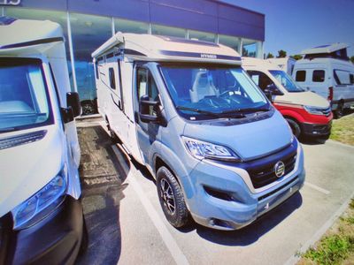 une petite camionnette bleue garée sur un parking, à côté d'autres véhicules