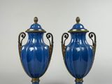 une paire de vases bleus munis d'anses, posés sur des socles, sur une surface blanche
