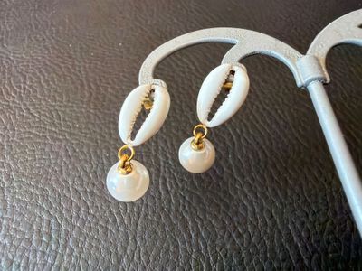 paire de boucles d'oreilles en coquillage blanc rehaussées de touches dorées sur un fond en cuir noir