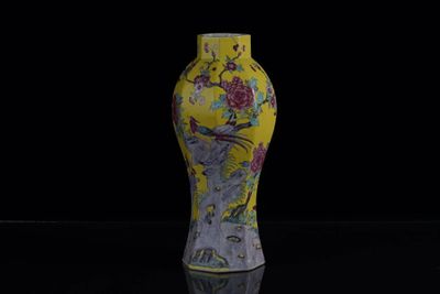 un vase jaune orné de fleurs, posé sur une surface noire