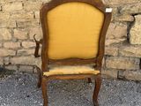 an old wooden chair with a yellow upholstered seat in front of a stone wall
