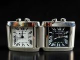 two silver square watches sitting side by side on a black surface