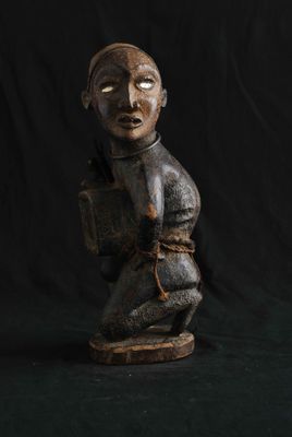 une statue en bois représentant un homme portant un sac à dos sur le dos