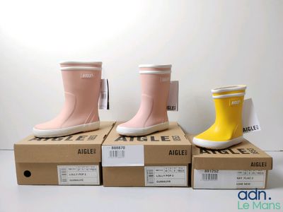 trois paires de bottes de pluie roses et jaunes posées sur des cartons
