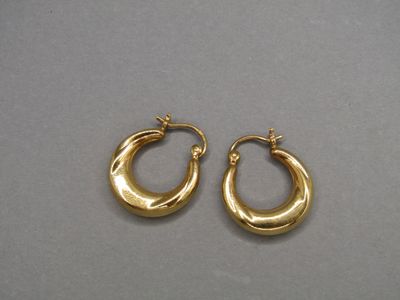 une paire de boucles d'oreilles créoles en or posées sur une surface grise
