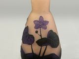 a vase with a purple flower on it sitting on a table