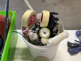 a bucket full of tape, scissors and other items on a table