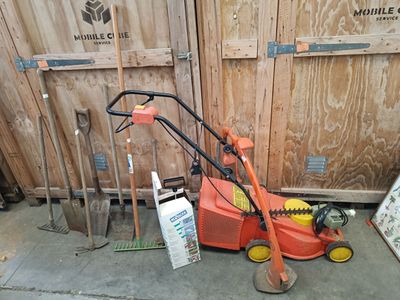 a lawn mower sitting on the sidewalk next to a pile of tools