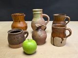four different vases and a green apple on a table