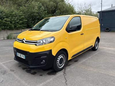La camionnette jaune est garée sur un parking, avec des arbres en arrière-plan.