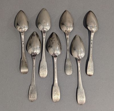 six cuillères en argent sont alignées sur une surface grise
