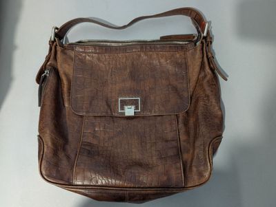 sac à main en cuir marron accroché à un mur blanc, avec un mur blanc en arrière-plan