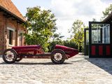 a red car parked on a cobblestone road in front of a brick building
