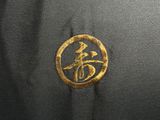 the back of a black jacket with a gold embroidered logo