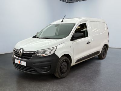 La camionnette blanche est garée dans une grande pièce au sol noir.