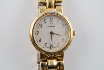 une montre-bracelet en or avec un cadran blanc sur une surface blanche