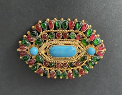 a close up of a broochle with a blue stone surrounded by green and red beads