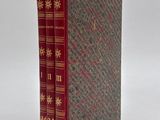 an old book with a red cover sitting on top of a white surface
