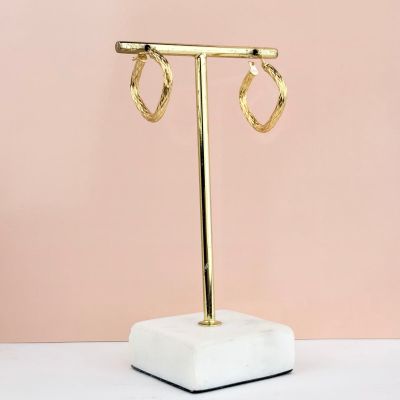 a pair of gold hoop earrings on a marble stand against a pink wall