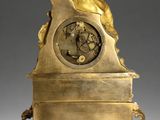 a gold clock with a woman sitting on top of it