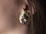 La femme porte une paire de boucles d'oreilles en or ornées de pierres colorées.