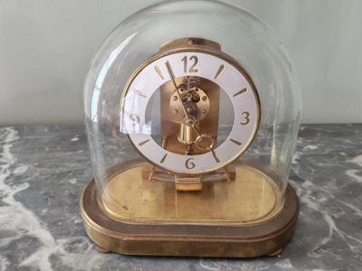 Pendule KUNDO en métal doré sous son globe. 24 x 23 cm. max.