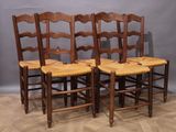 Quatre chaises en bois sont alignées contre un mur gris.