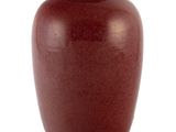 un vase rouge muni d'un couvercle, posé sur une surface blanche