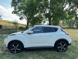 the white nissan juke suv is parked in a grassy field