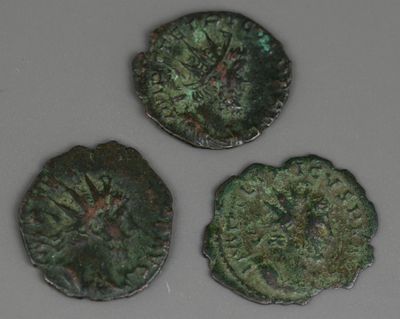 trois pièces de monnaie romaines anciennes posées sur une surface blanche